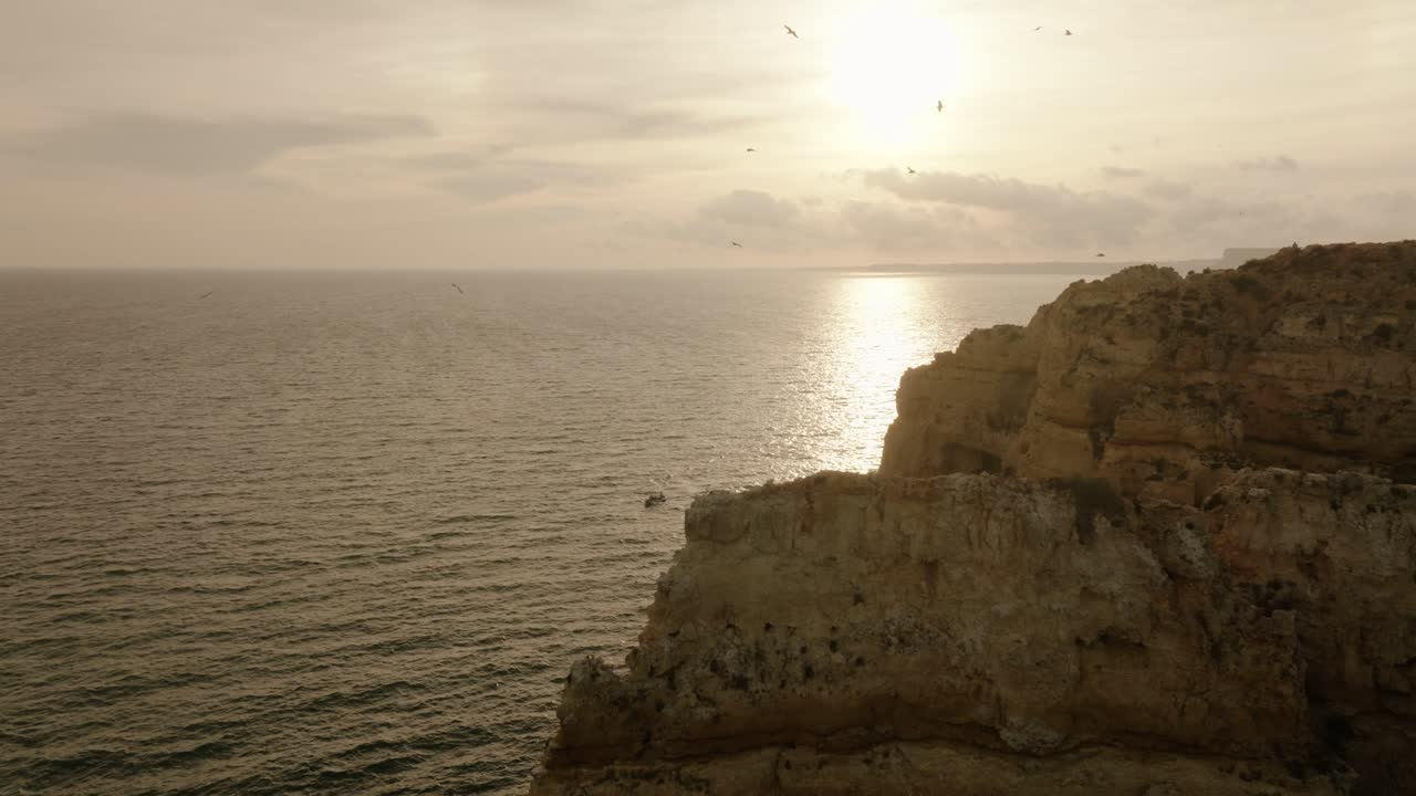 Aerial view of sunlit cliffs and calm ocean in Algarve, Portugal, captured during golden hour with soft natural light
