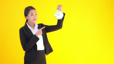 a young businesswoman on a solid background raises a clock then points to it