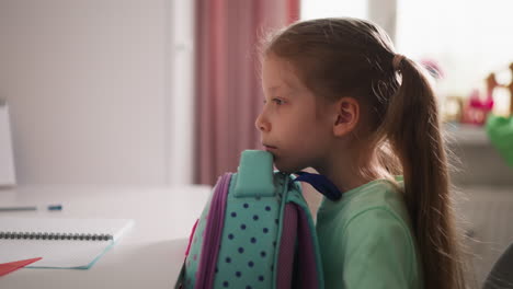 pretty girl pupil opens rucksack and looks inside at desk