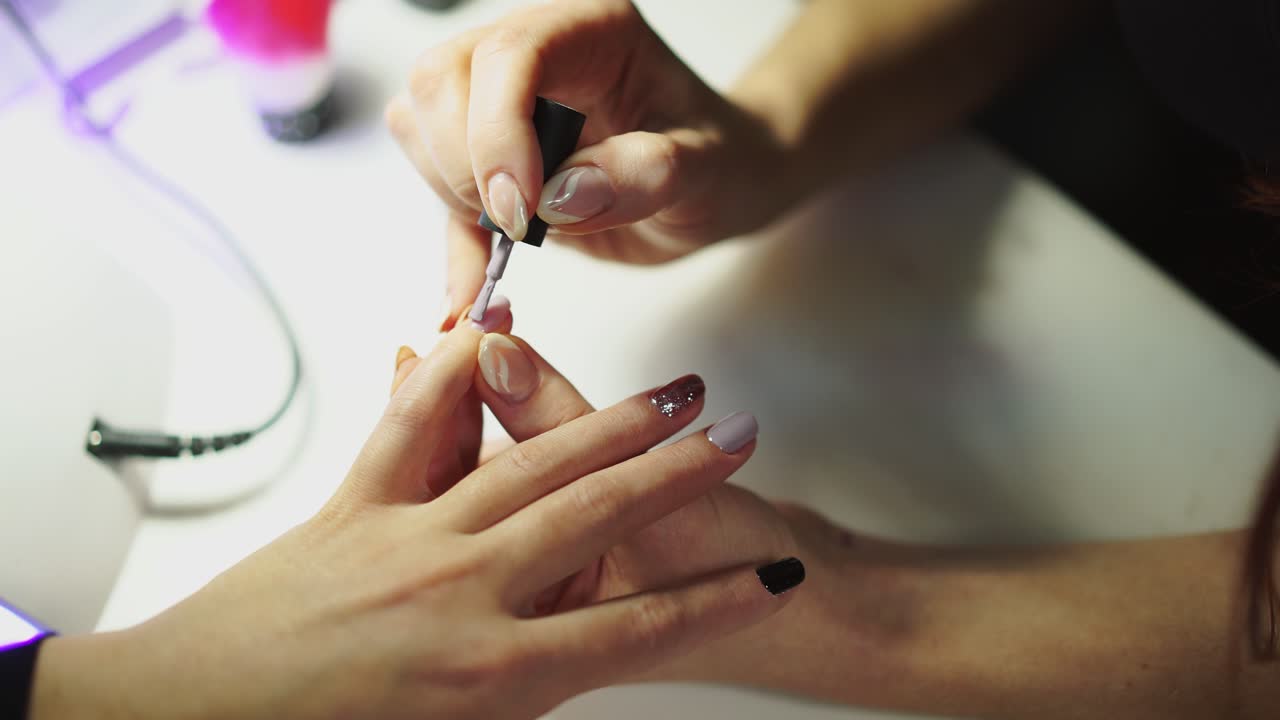 Close-up of female hands making manicure with nail lacquer in beauty salon. Woman hands receiving a manicure by a beautician. Woman is getting nail manicure, spa treatments