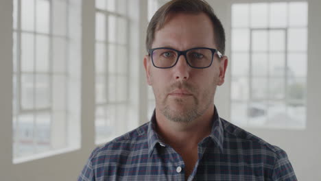 portrait of young caucasian man looking serious at camera in apartment background wearing glasses