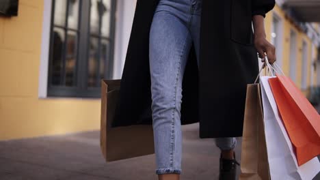 Lose-Up-Of-Woman-Legs-Wearing-Stylish-Black-Coat-And-Jeans-At-Day-Time-Hold-Colored-Shopping-Bags-After-Big-Shopping-Day