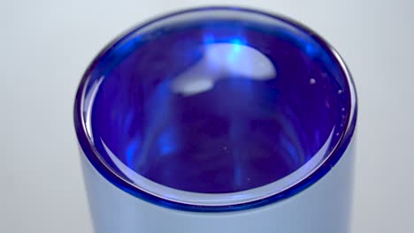 selective focus close up view of water droplet falling into transparent glass producing splash and ripples in slow motion.