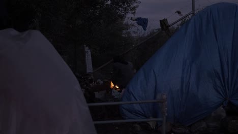 an afghan woman sits by fire moria refugee camp