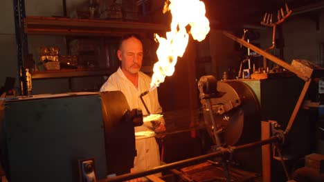 mature male worker lighting glass blowing torch in glass factory 4k