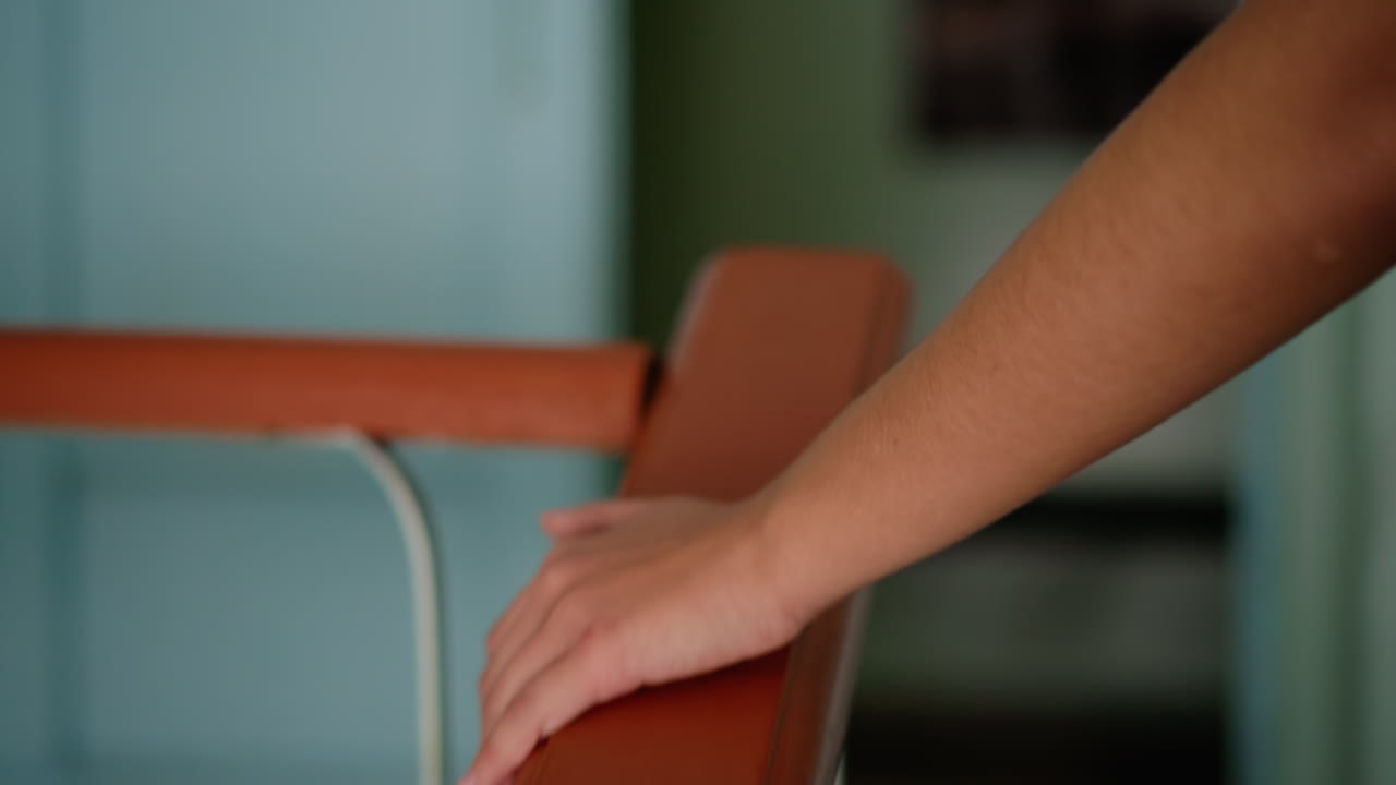 Close view of human hand moving along glossy staircase handrail with blurred background, soft light highlighting gesture of contact and support, evoking sense of balance, safety, motion