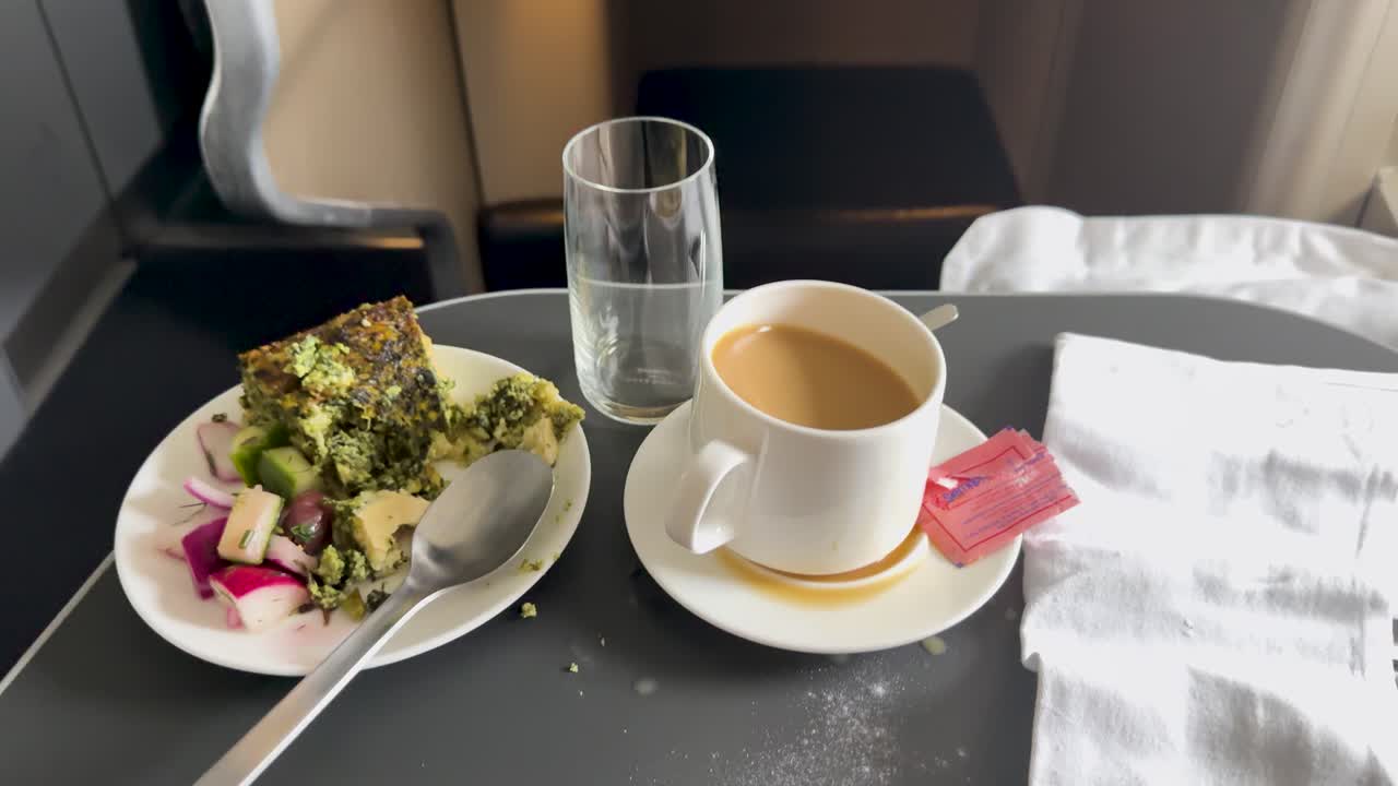 Coffee spills on airplane tray table during turbulence, with meal, glass, and natural daylight