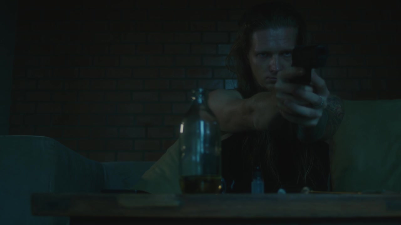 Tattooed Man Cleaning and Aiming a Handgun in a Dimly Lit Room