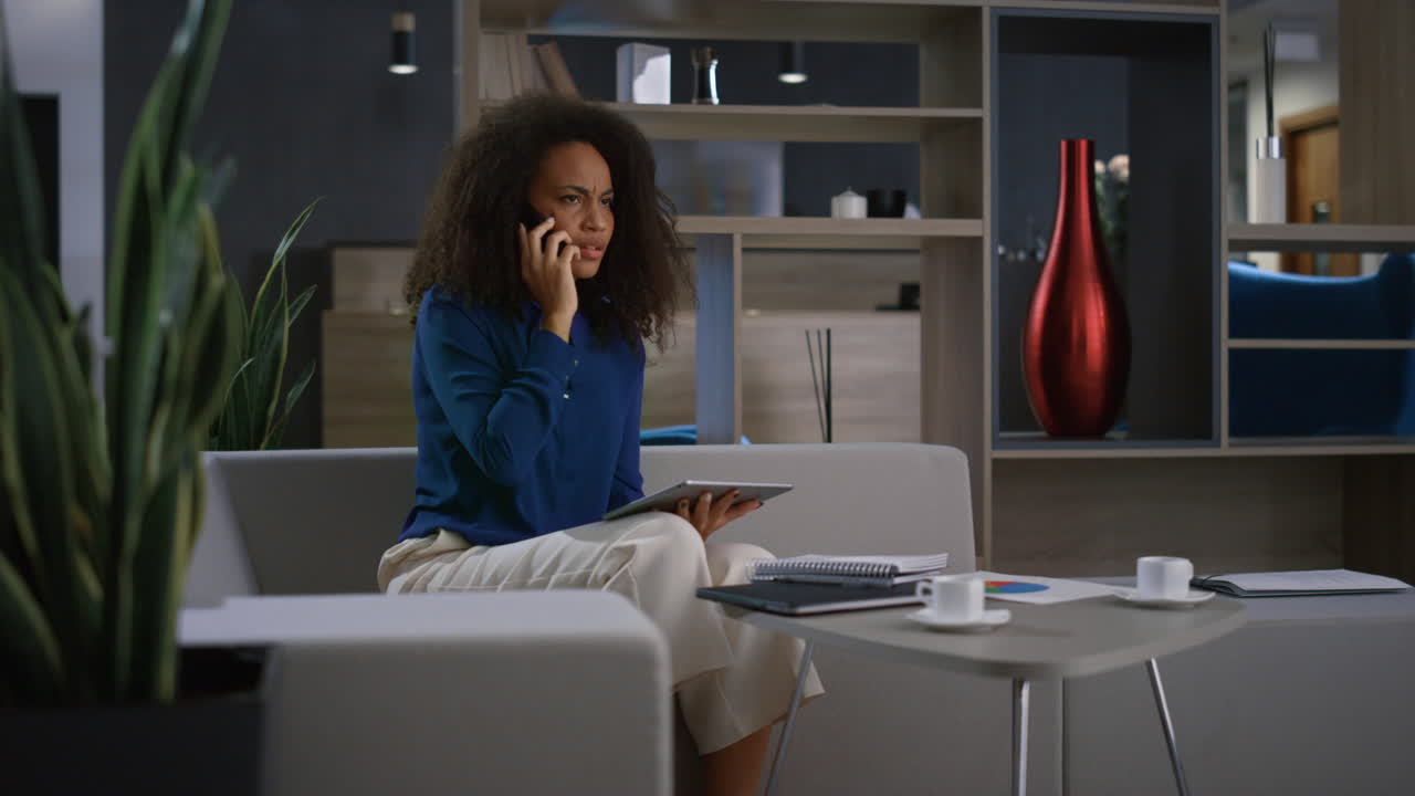 Giovane donna d'affari afroamericana che parla al telefono in ufficio. Concetto di lavoro remoto.