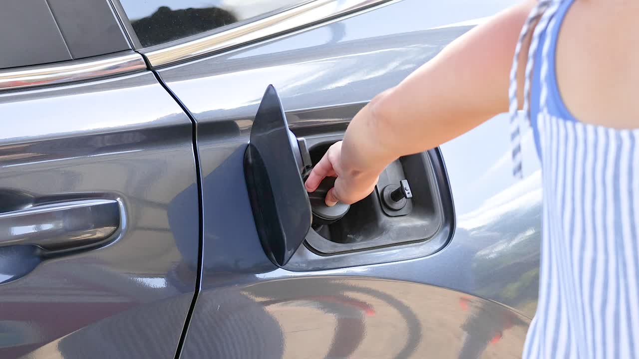 A person opens a car's fuel tank cap in bright daylight at Phuket's Khao Rang Viewpoint