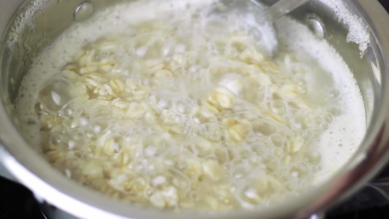 usando una cuchara de metal para revolver la avena hirviendo a fuego lento en una cacerola de metal en una placa de convección