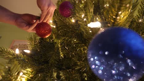 person decorates a christmas tree with pretty sparkling ornaments