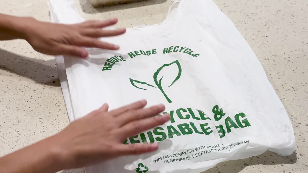 Hands interact with a recyclable bag on a kitchen countertop. Bright lighting highlights the bag's eco-friendly message