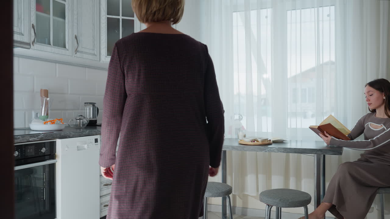 집주인은 딸과 함께 주방에 들어와 책상에 앉아 소설을 읽고, 편안한 가정 환경에서 어머니와 딸에 부드러운 초점을 맞추고, 차분한 환경에서 따뜻함과 가족 상호 작용을 불러일으니다.