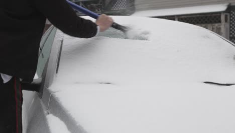 man wearing black jacket slowly scraping ice on the car window during winter day - closeup shot