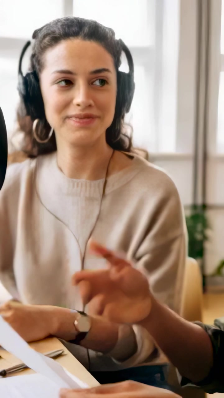 Vertical video: Leaning as hand entering script, host with headset and hoops reading and nodding