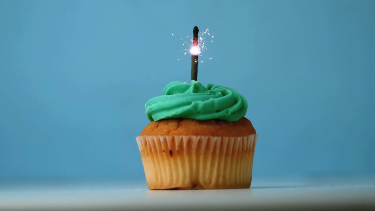 Lighting sparkler atop cupcake shooting sparks as gold confetti drifting down celebrating birthday