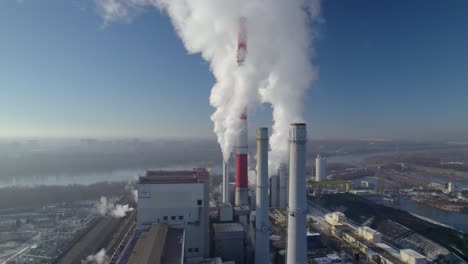 aerial close orbit shot of a coal-fired heating power station with thick white smoke coming from the chimneys