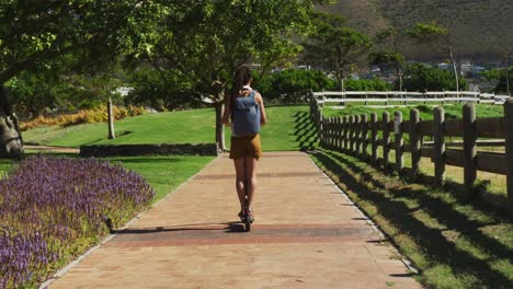 african american woman wearing backpack riding scooter in park