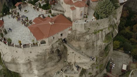 aerial view over the monastery varlaám full of tourists, in meteora, greece - rising, high angle, drone shot