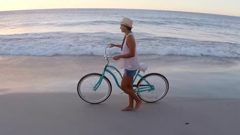 beautiful young woman walking on the beach with a bicycle