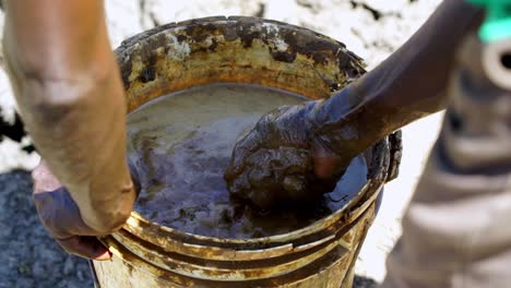 manos masculinas preparando barro en un cubo para montículos de termitas en un pozo de agua para animales en uganda