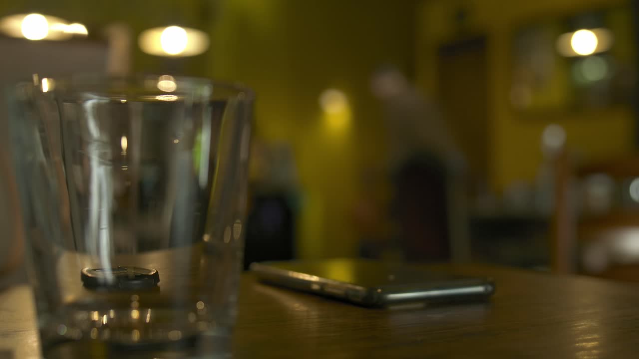 Static shot of a glass on a table with people moving in the background.