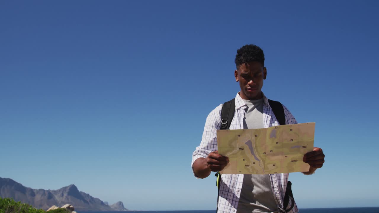Afroamerikansk mand, der vandrer og læser et kort i et kystlandskab.