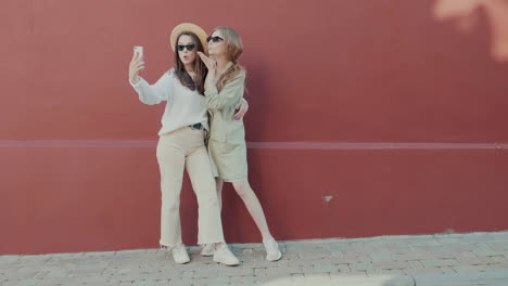 two women taking a selfie by a red wall