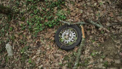 discarded-car-wheel-tire-lying-in-forest-ground,-ecological-disaster,-shot-up-looking-down-to-the-ground