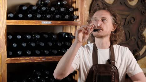 authentic shot of successful male sommelier is tasting a flavor and checking white wine quality poured in transparent glass in a wine cellar.