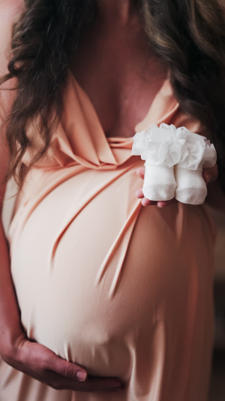 Close up of a pregnant woman holding white baby socks on her belly. Vertical