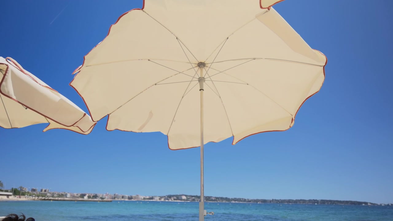 Grandi ombrelloni bianchi da spiaggia visti dal basso contro un cielo estivo limpido e azzurro.