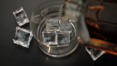 whiskey poured over ice cubes in a glass