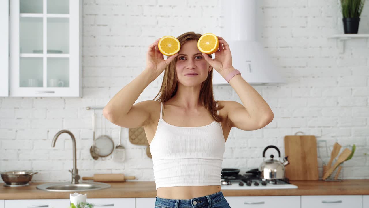 A positive smiling girl with orange slices in her hands closes her eyes