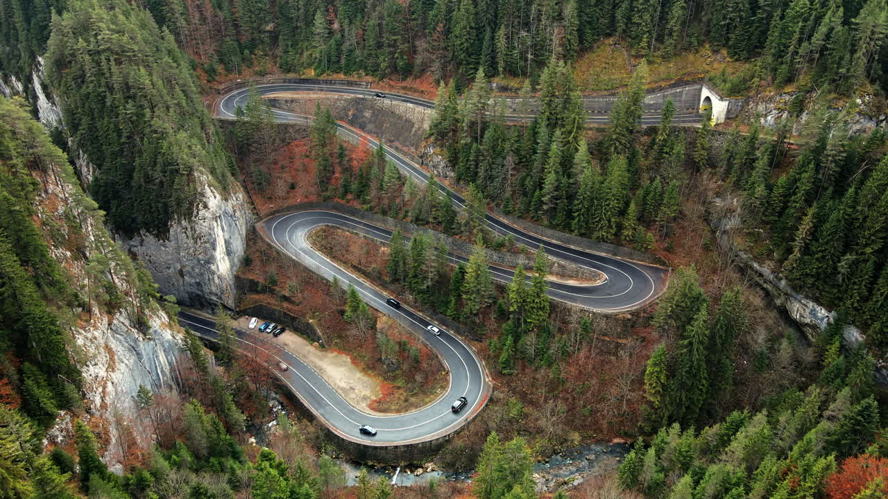 Aerial drone view of nature in Romania. Carpathian mountains, serpentine road with cars in the valley, rocky hills covered with lush forest