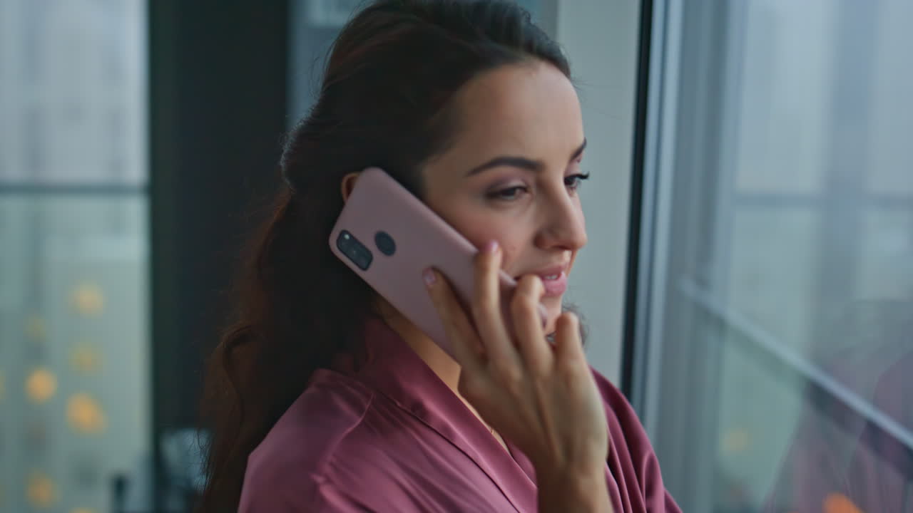 ama de casa sonriente hablando por teléfono móvil en las ventanas del dormitorio de primer plano. llamada de la mujer
