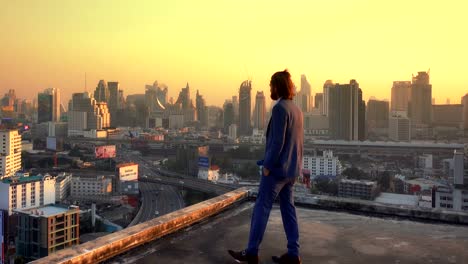 western businessman walking to the edge of rooftop in front of bangkok city at sunset in business concept. thailand