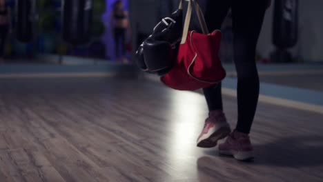 close up view of legs of young fit woman entering a fitness club with a bag and boxing gloves and preparing for the training in a