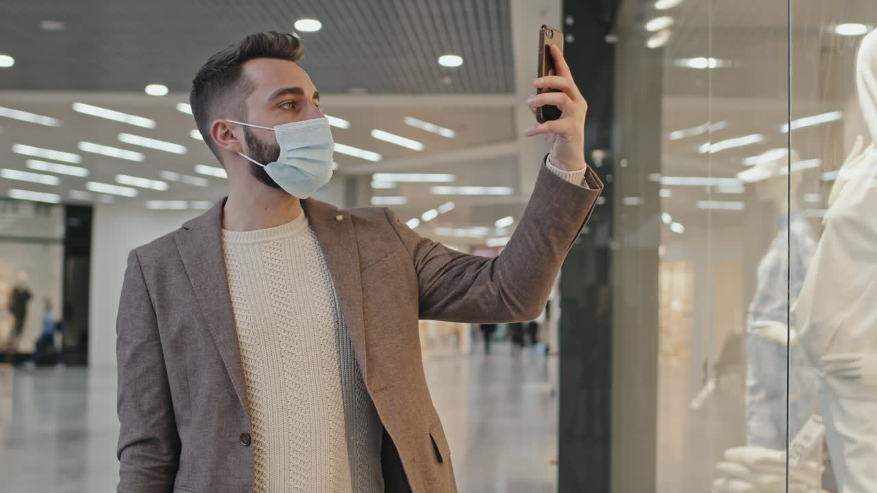 Man In Face Mask With Smartphone Doing Clothes Shopping