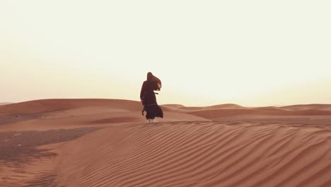 mujer musulmana de pie cerca de la mezquita en el desierto. viento fuerte oriente medio paz sin guerra