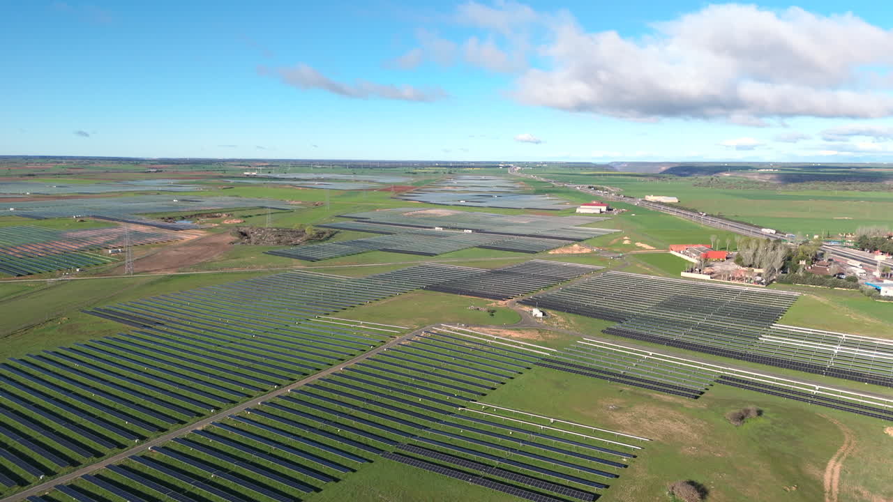 Drone shot of large-scale solar power plant with vast green landscape on clear sunny day. Renewable energy concept