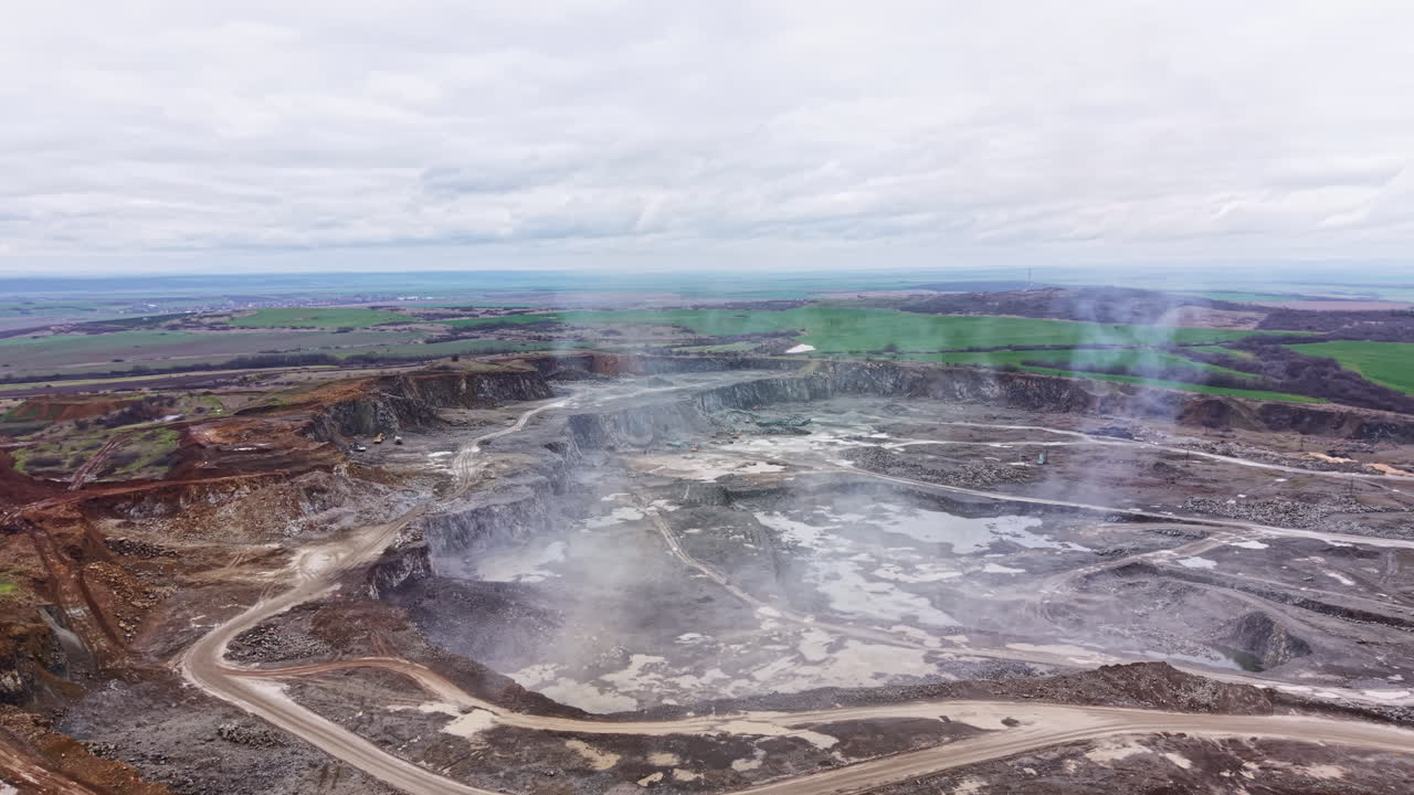 Granite quarry shows large open pit and machinery in action during cloudy weather with green fields in the background