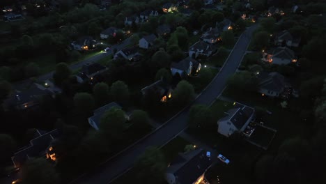 glowing houses and homes in quiet american neighborhood. aerial top down flyover. large single family houses at night. villas and apartments in suburbia.