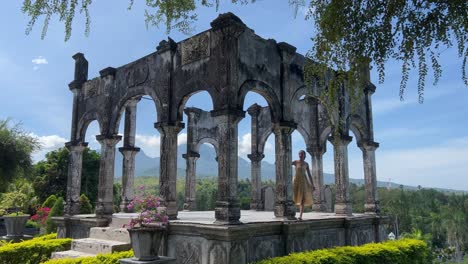 romance encantador en el palacio acuático de taman ujung: una joven vestida explora la histórica estructura de piedra con pilares en el este de bali