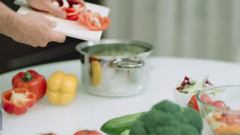 closeup man hands putting sliced peppers into cooking pot in slow motion.