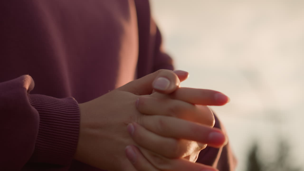 vista de cerca de la mano de una persona con ropa marrón trabajando en el estiramiento de la muñeca con los dedos entrelazados, con la luz del sol creando un reflejo brillante en las manos