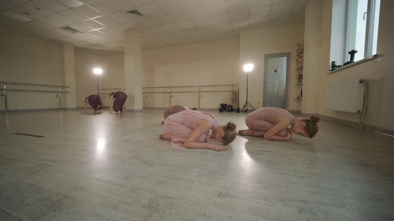 un grupo de jóvenes estudiantes de ballet con ropa de baile negra practicando posiciones en un amplio estudio de ballet con pisos de madera y barras montadas en la pared. expresiones enfocadas y movimientos sincronizados.
