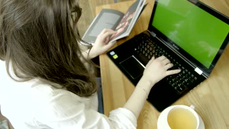 mujer morena usando una computadora portátil con pantalla verde, bebiendo té en una cafetería. vista trasera. llave de croma