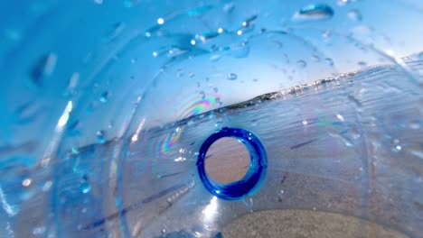 la botella de plástico desechada en la playa descuidadamente es barrida para ver por las olas y la marea - como se ve desde el interior de la botella